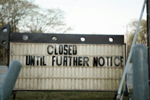 A white & black wooden sign that says "Closed Until Further Notice".