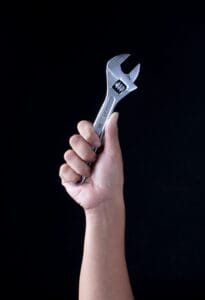 A hand holding a wrench triumphantly on a black background. Photo by Recha Oktaviani on Unsplash