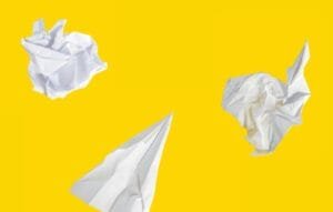 Crumpled paper and a paper airplane on a yellow background. Photo by Matt Ridley on Unsplash