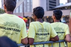 Three people in yellow shirts with "Volunteers" written on the back. Photo by Rashpal Singh on Unsplash
