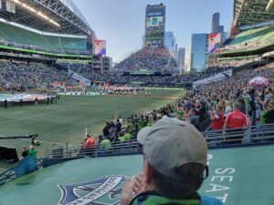 The prematch presentation for a Seattle Sounders soccer match in 2018. People in the stadium watch as the team marches on the pitch.